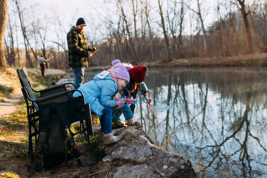 Young girls on family fishing trip dangling poles in river