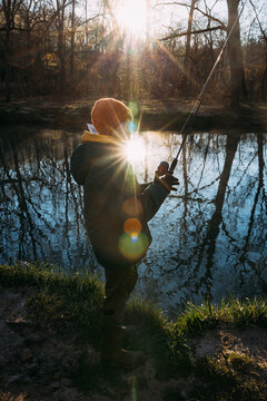 Child standing on riverbank early morning with fishing pole