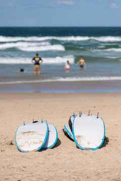 Beginner surfboards on Sand with Kids in Water in background