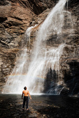 Man gazing at tall waterfall with rainbow