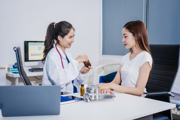 Fototapeta premium An Asian woman sits at a table consulting with a female doctor. They discuss her symptoms related to stress and depression. The doctor listens attentively and recommends treatment and medication