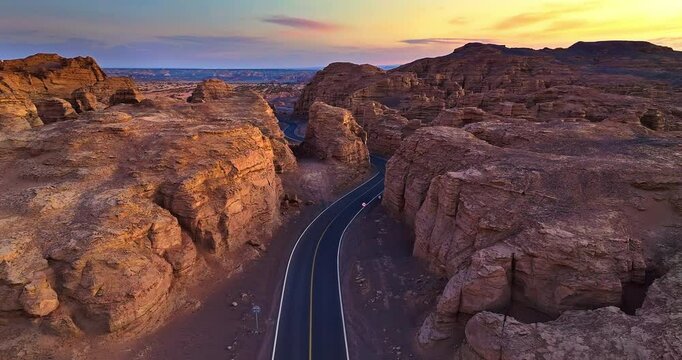 Aerial shot of a winding asphalt road through dramatic yardang landform rock formations at sunset in Xinjiang, China.