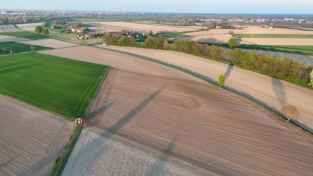 Sunset-lit tractor moves slowly across alternately plowed and smooth soil creating long diagonal shadows and accentuating rippled field patterns near Olza di Castelvetro Piacentino in slow motion