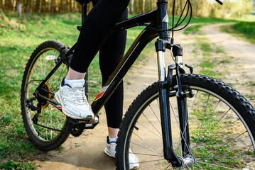 Fototapeta premium Female cyclist holding the handlebars of a mountain bike is going to ride outdoors against the background of a spring forest.