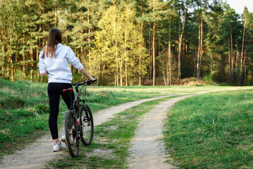 Obraz premium Female cyclist holding the handlebars of a mountain bike is going to ride outdoors against the background of a spring forest.