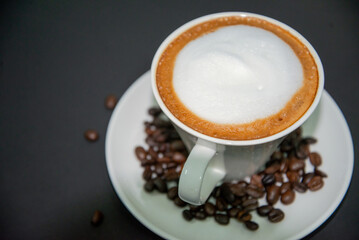 Close-up top view of a white cup of coffee with foam on a saucer with coffee beans, Coffee Break.