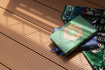 A pile of the holy Quran with Arabic calligraphy with natural daylight and prayer mat below it on...