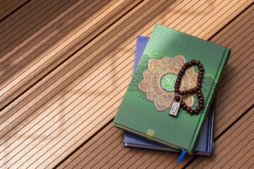 A pile of the holy Quran with Arabic calligraphy and wooden beads or tasbih with natural daylight...