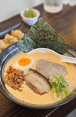 Spicy Ton Ton ramen in orange chilli soup serving with egg on black bowl
