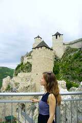 Visiting the most scenic places in Serbia: portrait of a woman standing at the viewpoint of the Golubac fortress. A female tourist against the background of the towers of a medieval European castle