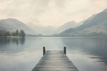 Minimalist photograph of an old wooden dock leading into calm waters and majestic muted grey mountains