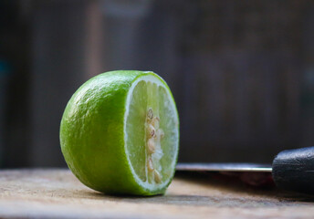 Lime halved on a wooden cutting board with a knife next to it. Food ingredient concept, sour...