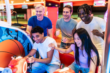Happy multiethnic friends playing arcade basketball game together