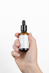 Naklejka premium Mockup of a glass bottle with a dropper. In a woman's hand. Cosmetics hair oil. Empty label. Place for an inscription and logo.