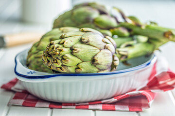 Ripe artichokes plant in bowl on white table.