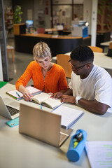University students reviewing textbook together in library