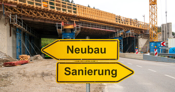 Zwei Wegweiser zeigen in unterschiedliche Richtungen mit dem Aufdruck Neubau und Sanierung vor einer Autobahnbrücke im Bau - FOTOMONTAGE