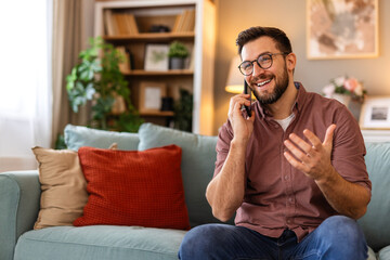 Obraz premium Man sitting on a sofa, talking on the phone, enjoying a relaxed moment at home. Combining comfort and communication, he embraces a peaceful break in his daily routine.