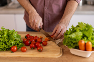Man chopping vegetables in a kitchen, preparing ingredients for a meal. He is focused on the task, enjoying the process of cooking, with a relaxed and organized kitchen environment.