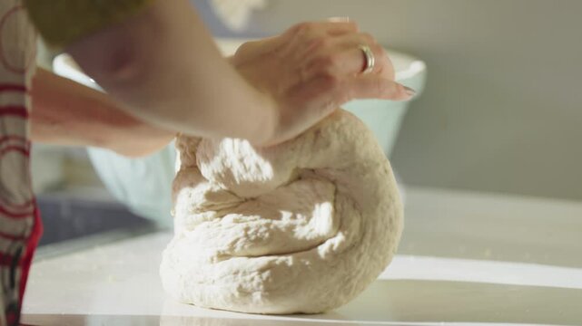 A home baker kneads pliant dough, preparing for fresh bread in a rustic kitchen.