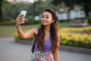 Young woman takes a selfie in a park during daylight, enjoying a moment outdoors with flowers