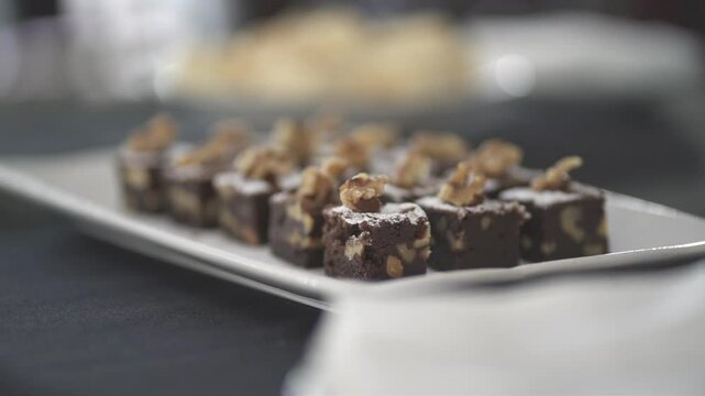 Close-up of arranged in rows chocolate brownie fudge with walnut pieces on a serving plate.