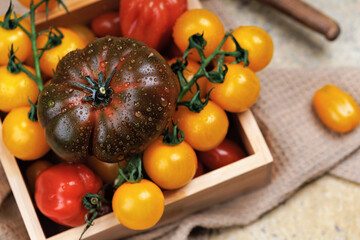 Assorted cherry and heirloom tomatoes in wooden box on rustic fabric with water drops