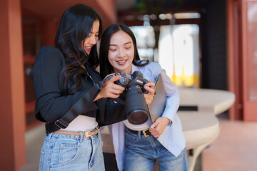 Two young female photographers are smiling while reviewing photos they just took on their professional dslr camera, sharing a moment of creative collaboration and passion for photography