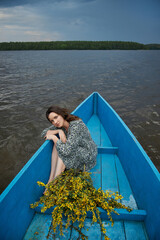young woman relaxes in a vibrant blue boat, resting her chin on her arms. She is surrounded by...