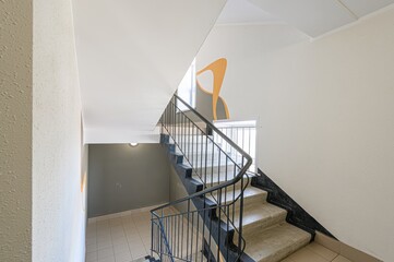 interior apartment public place, view of stairwell with concrete steps, dark railing, and white walls. An orange abstract design is on one wall.