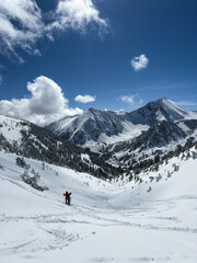 A person is walking on a snowy mountain with a beautiful blue sky in the background. Concept of adventure and tranquility, as the person enjoys the serene and picturesque landscape