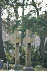 Two old gravestones with crosses stand in a peaceful, wooded cemetery.