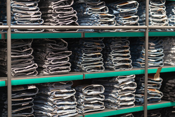 Many stacks of folded jeans trousers are filling shelves with green borders, offering various...