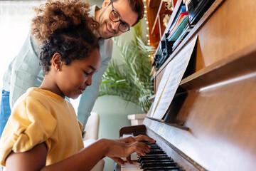 Happy man, pianist teacher giving piano lesson to a little school girl, playing music together