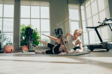 Fototapeta premium Beautiful girl and her cute little daughter smile while playing yoga, sport workout together at the gym