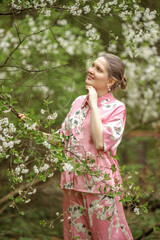 Fototapeta premium Young woman in pink national costume of Japan, walking in a garden with blooming sakura