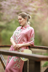 Naklejka premium Young woman in pink national costume of Japan, walking in a garden with blooming sakura