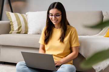 Remote growth and self-reflection. Young Latina Indian woman in her 20s using laptop on sofa for online therapy or studying, balancing mental health and education in a relaxed home vibe