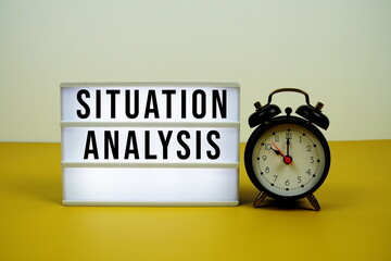 Situation Analysis text on LED lightbox with alarm clock on yellow background