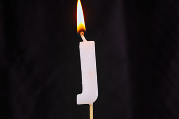 close up on a white letter J birthday candle with fire on a black background.
