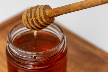 Close up shot of honey dripping from honey dipper in a jar of honey