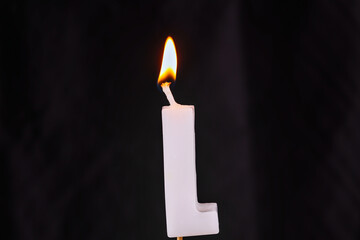 close up on a white letter L birthday candle with fire on a black background.
