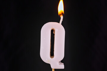 close up on a white letter R birthday candle on a black background.
