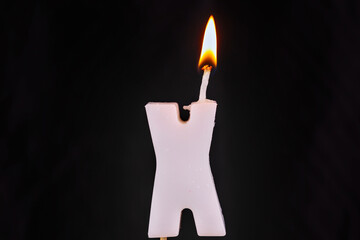 close up on a white letter X birthday candle with fire on a black background.
