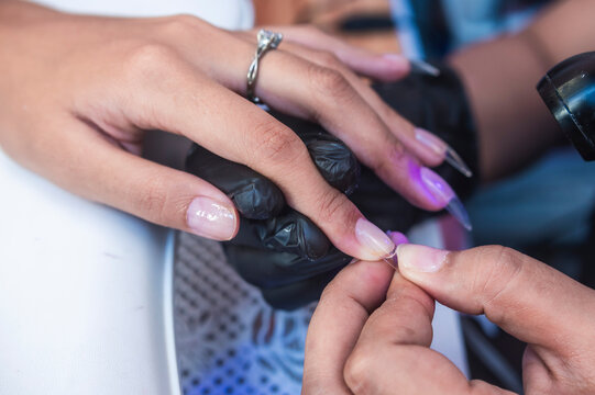 Close-up of a beauty technician pressing a soft gel tip onto the nail surface using adhesive during a manicure or nail art session in a salon environment.