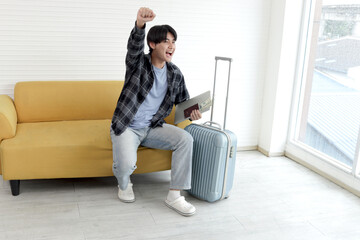 Happy young Asian male tourist with passport and money planning for his journey. Cheerful traveler...