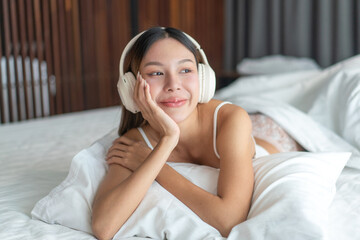 Asian woman relaxing on bed with headphones. Young female enjoying peaceful moment and listening to...
