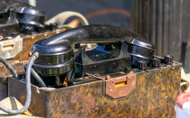 set of vintage military field telephones from World War II, displayed on a table outdoors. The devices show significant rust and wear, emphasizing their age and authenticity. A great visual for themes