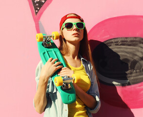 Stylish young girl with skateboard in glasses, modern teenager girl posing against the graffiti wall