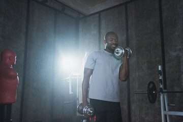 Fitness workout in gym. African American man bodybuilder picking up dumbbells in gym. Workout...